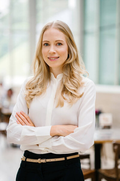 Professional portrait head shot of a Caucaasian woman expatriate working in Singapore, Asia. She is middle-aged in her 30's, attractive, blond and beautiful in a crisp white shirt in an office.