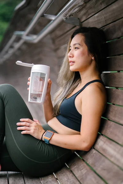 Portrait of an attractive, young Chinese Asian woman dressed in sporty, active wear with water  in green public park in Singapore during the day on the weekend.