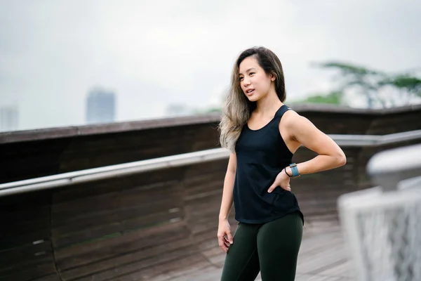 Portrait of an attractive, young Chinese Asian woman dressed in sporty, active wear in  public park in Singapore during the day on the weekend.