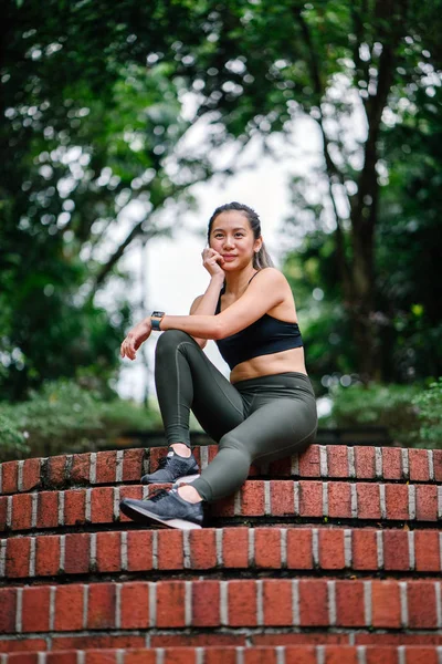 一个迷人的 年轻的中国亚裔女子的肖像 穿着运动 积极穿在一个郁郁葱葱的 绿色的公共公园在新加坡的一座桥上周末的一天 — 图库照片