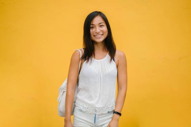 Konforlu giyinmiş ve sarı bir arka plan bir stüdyoda kameraya gülümseyen bir atletik, şirin Çinli Asyalı kız portresi.