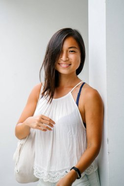 Stüdyo bir şirin, atletik ve tabaklanmış Çinli Asyalı kadın portresi. O beyaz bir arka plan karşı duruyor ve konforlu için sıcak hava rahat kıyafetler giymiş gibi gülümsüyor.