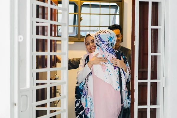 Muslim husband and wife couple greet a guest at their door and invite her in to celebrate Hari Raya, a Muslim celebration of love and forgiveness. They are overjoyed to see one another.