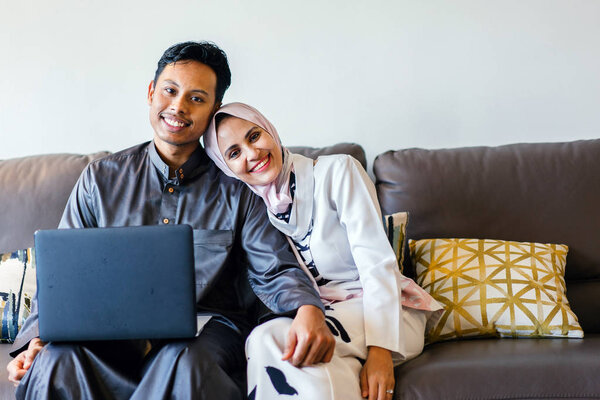 portrait of a Muslim Malay couple at home with laptop during the Muslim festival of Hari Raya in Singapore, Asia.