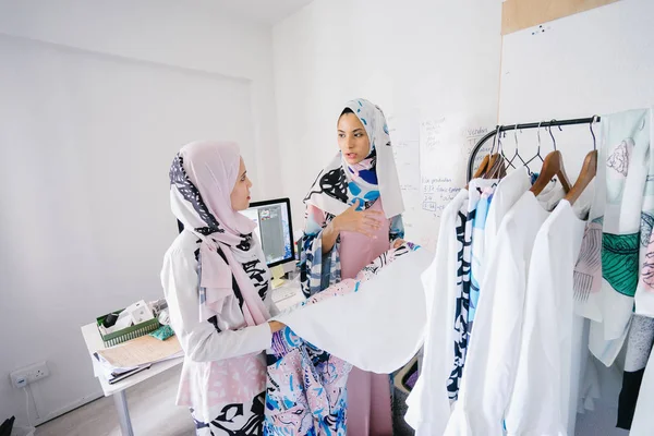 Two young and attractive Muslim women entrepreneurs are having a business discussion in a retail office. They are both wearing head scarves (hjiab) and having an intense conversation about their work.