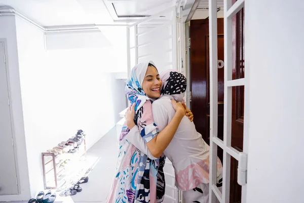 Muslim woman greeting a guest at the door and invite her in to celebrate Hari Raya, a Muslim celebration of love and forgiveness. They are overjoyed to see one another.