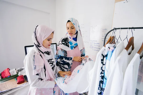 Two young and attractive Muslim women entrepreneurs are having a business discussion in a retail office. They are both wearing head scarves (hjiab) and having an intense conversation about their work.