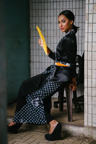 Fashion portrait of an attractive, intense Muslim model. She is wearing a silky kimono , she sits in a chair on a street in Asia.