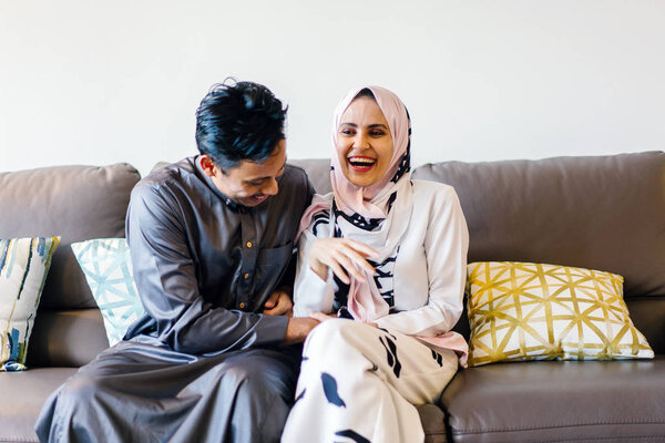  portrait of a Muslim Malay couple at home during the Muslim festival of Hari Raya in Singapore, Asia. They are sitting on their home couch 