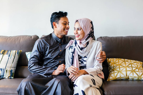  portrait of a Muslim Malay couple at home during the Muslim festival of Hari Raya in Singapore, Asia. They are sitting on their home couch 