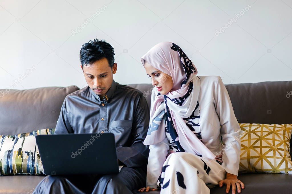 portrait of a Muslim Malay couple at home with laptop during the Muslim festival of Hari Raya in Singapore, Asia.