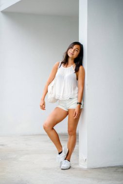 Stüdyo bir şirin, atletik ve tabaklanmış Çinli Asyalı kadın portresi. O beyaz bir arka plan karşı duruyor ve konforlu için sıcak hava rahat kıyafetler giymiş gibi gülümsüyor.