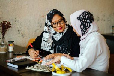Two attractive Muslim women entrepreneurs are having a business discussion in coworking space. They are both wearing head scarves (hjiab) and having an intense conversation about their work. clipart