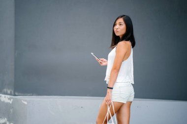 Gri bir arka plan karşı sokakta yürürken şirin, atletik, yanık tenli Asyalı Çinli bir kız portresi.