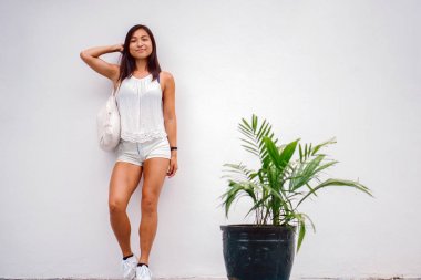 Bir sokakta bir duvara yaslanmış atletik, tabaklanmış, minyon ve şirin Çinli Asyalı kadın 