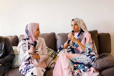 İki Müslüman kadınların başörtüsü karaoke ev eğlence sistemlerinde Hari Raya üzerinde şarkı söylüyorlar ve birbirlerinin şirket zevk.