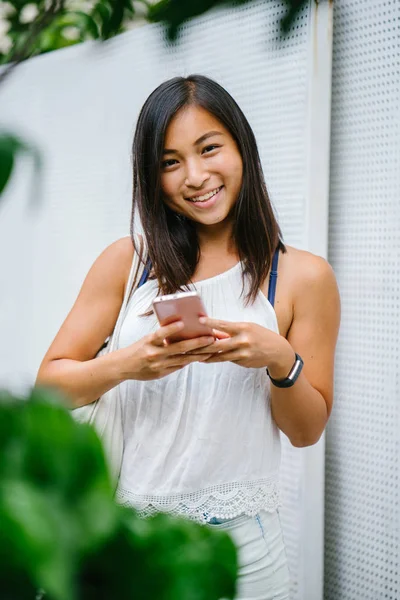 Athletic, toned and tanned Chinese Asian girl smiling as she texts on her mobile phone in the day. She is relaxed and having fun.