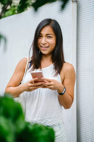 Athletic, toned and tanned Chinese Asian girl smiling as she texts on her mobile phone in the day. She is relaxed and having fun.