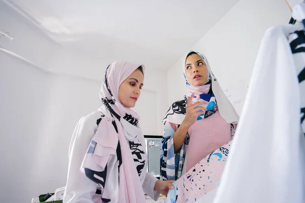 Two young and attractive Muslim women entrepreneurs are having a business discussion in a retail office. They are both wearing head scarves (hjiab) and having an intense conversation about their work.