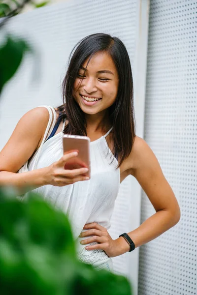 Athletic, toned and tanned Chinese Asian girl smiling as she texts on her mobile phone in the day. She is relaxed and having fun.