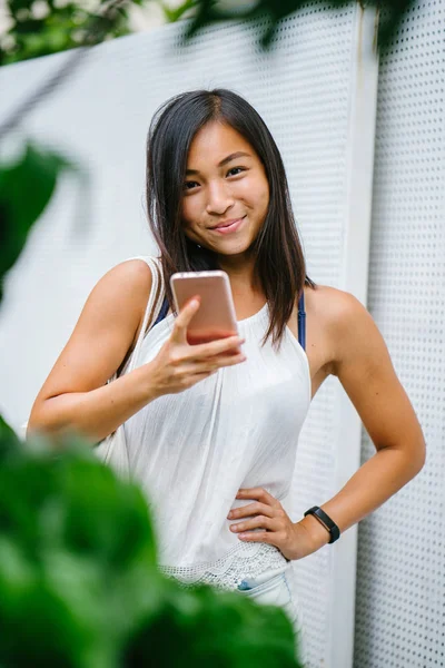 Athletic, toned and tanned Chinese Asian girl smiling as she texts on her mobile phone in the day. She is relaxed and having fun.