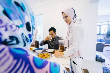 Müslüman aile yemek için evde oturur. Baş eşarp ve bir adam iki kadın sessiz bir yemek keyfini çıkarın..