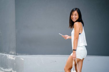 Gri bir arka plan karşı sokakta yürürken şirin, atletik, yanık tenli Asyalı Çinli bir kız portresi.