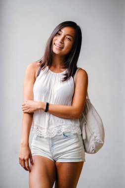 Stüdyo bir şirin, atletik ve tabaklanmış Çinli Asyalı kadın portresi. O beyaz bir arka plan karşı duruyor ve konforlu için sıcak hava rahat kıyafetler giymiş gibi gülümsüyor.