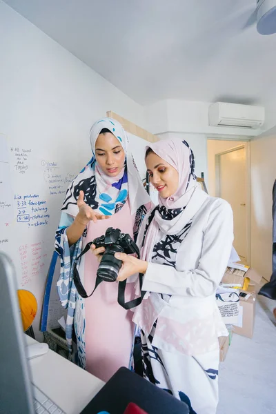 Two young and attractive Muslim women entrepreneurs are having a business discussion in a retail office. They are both wearing head scarves (hjiab). One of the women is in focus and talking intensely.