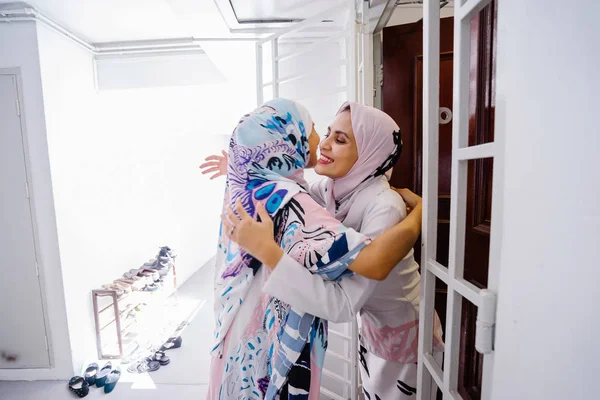 Muslim woman greeting a guest at the door and invite her in to celebrate Hari Raya, a Muslim celebration of love and forgiveness. They are overjoyed to see one another.
