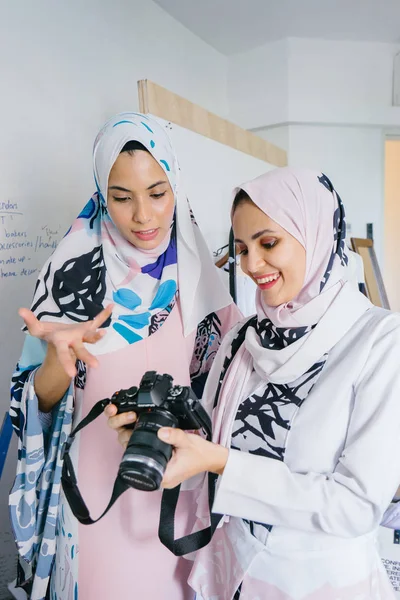 Two young and attractive Muslim women entrepreneurs are having a business discussion in a retail office. They are both wearing head scarves (hjiab). One of the women is in focus and talking intensely.