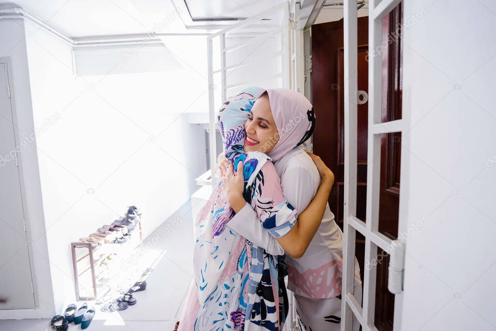 Muslim woman greeting a guest at the door and invite her in to celebrate Hari Raya, a Muslim celebration of love and forgiveness. They are overjoyed to see one another.
