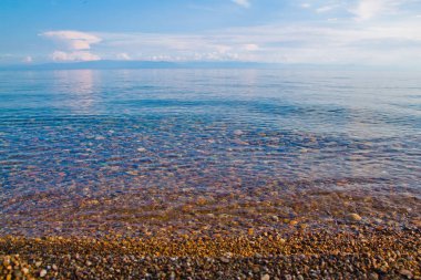 Net turkuaz su, taşlı plaj ve arka plan olarak mavi gökyüzü 