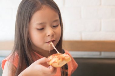 Sevimli mutlu küçük kız bir dilim peynirli pizza yiyor.