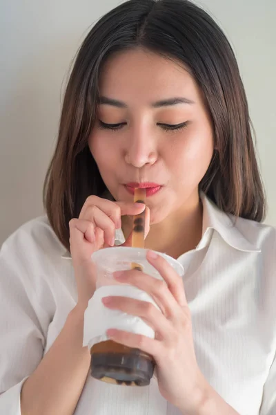 Happy smiling asian woman drinking iced bubble milk tea; aka boba tea, pearl milk tea, tapioca tea, asian exotic beverage concept; retouched image