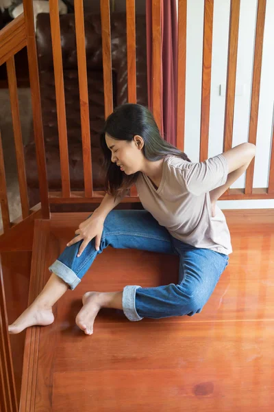 injured woman with back pain or injury; portrait of asian woman falling from staircase, having pain at her back or spine; concept of wound, bruise, injury, pain from accident