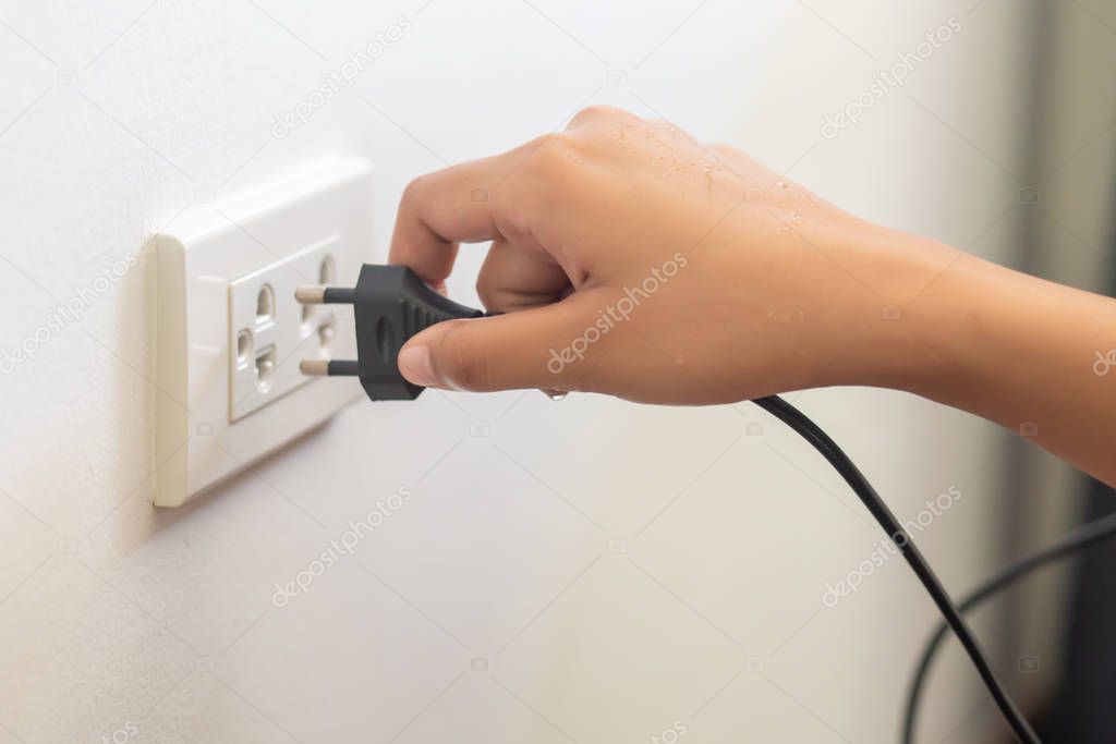 using electricity wall outlet with wet hand; electrocute danger concept