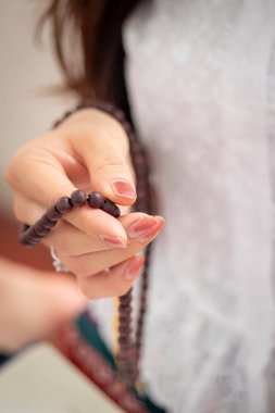 Dindar Asyalı Budist kadın elinde tespihle dua ediyor. Dişi Budist mürit meditasyon yapıyor, tespih boncuklarıyla ilahiler söylüyor tapınak salonundaki Buda heykeline dua ediyor.