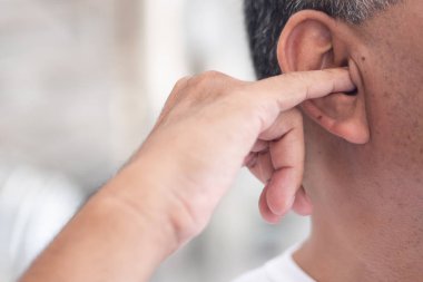 Kulak kiri, pis bir alışkanlıkla kulağını karıştıran adam; kulak kiri konsepti, sağlıksız alışkanlık, kötü kokulu kulak kiri...