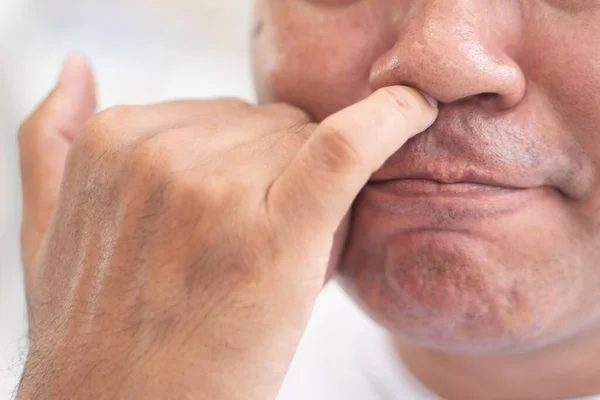 man picking his nose with nasty, dirty habit; concept of nose picking, unhealthy habit, bad manner with nose wax