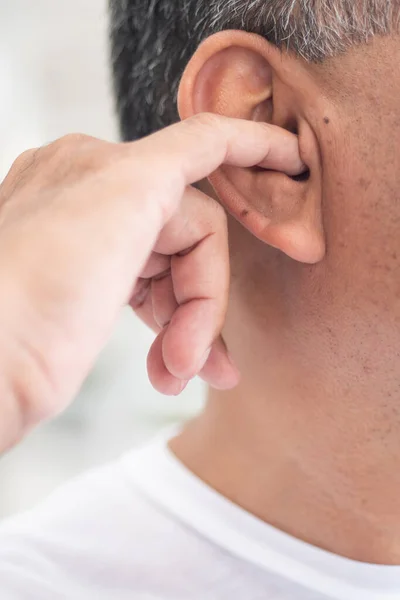 man picking his ear with nasty, dirty habit; concept of ear wax picking, unhealthy habit, bad manner with smelly, stinky ear wax