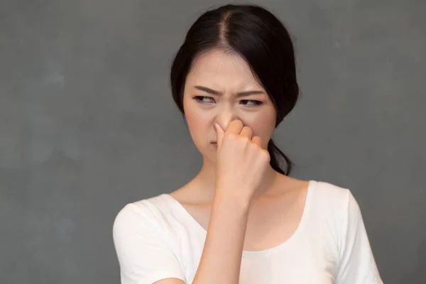 asian woman covering her nose for bad smell, concept of stink thing, bad breath, unpleasant smell, rotten food, odor, body bad smell; young adult Chinese asian woman model