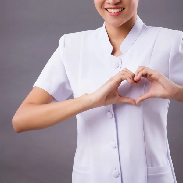 portrait of smiling asian woman nurse with heart hand sign isolated; friendly professional female nurse or medical worker with heart gesture for heart care service or body care or health care concept