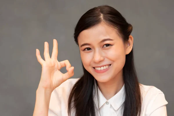 successful girl pointing ok hand sign; portrait of cheerful smiling woman pointing up approving, yes, ok, good, ok hand gesture; Chinese or east asian woman young adult model