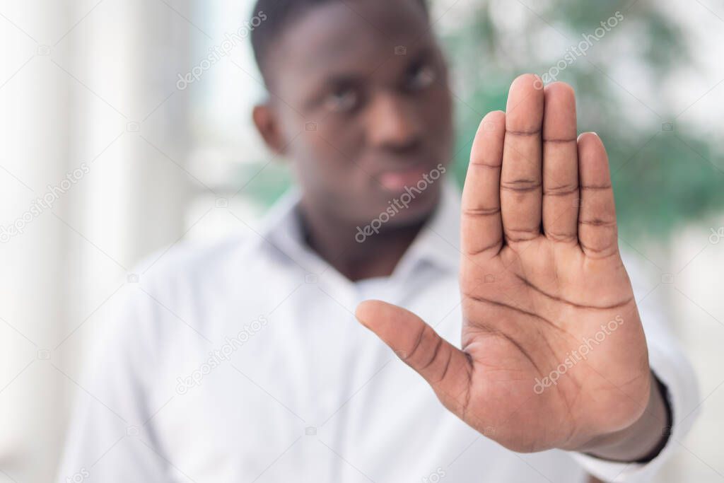 black African business man showing stop, halt hand gesture; concept of forbidden act, rejection, stop, halt, freezing, failure, no deal, deal breaker, no contract, sanction