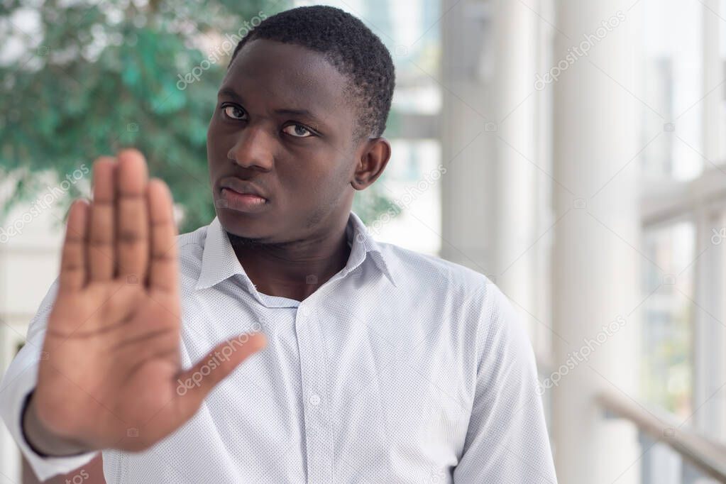 black African business man showing stop, halt hand gesture; concept of forbidden act, rejection, stop, halt, freezing, failure, no deal, deal breaker, no contract, sanction