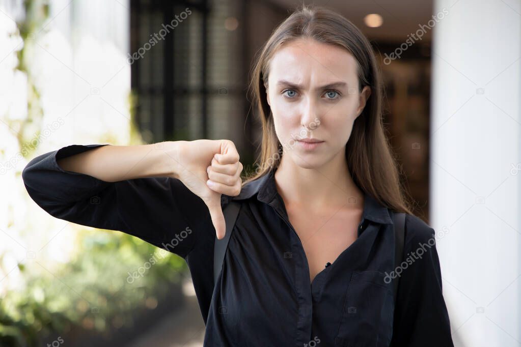 failed girl pointing thumb down; portrait of angry upset frowning woman pointing up disapproval, no, bad, failure, rejecting thumb down hand gesture; white caucasian woman young adult model
