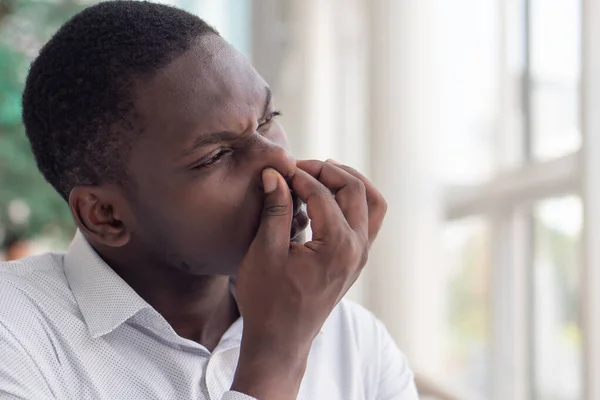 African black man covering his nose for bad smell; African black man plugging his nose to display concept of bad smell, bad breath, dirty or filthy thing, rotten stuff, gross fart smell