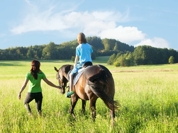 Montar a caballo Lecciones - Mujer liderando un caballo con un niño en S —  Fotos de Stock