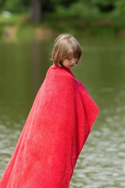 Menino de toalha vermelha em pé no molhe por um lago — Fotografia de Stock